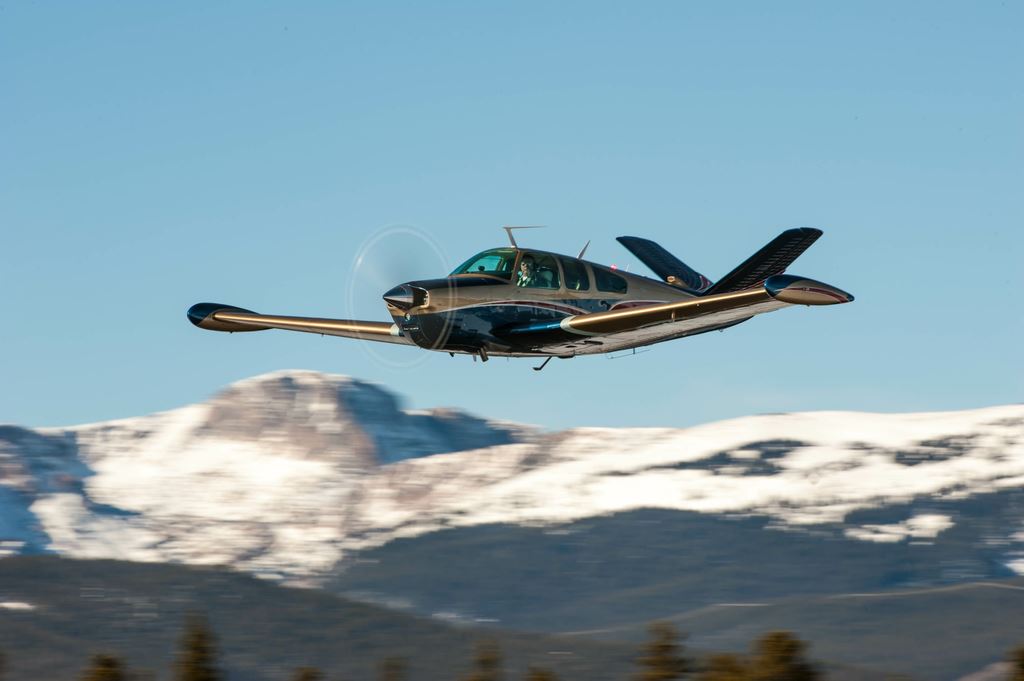 A Beechcraft Bonanza flying low past snow-covered Colorado mountains
